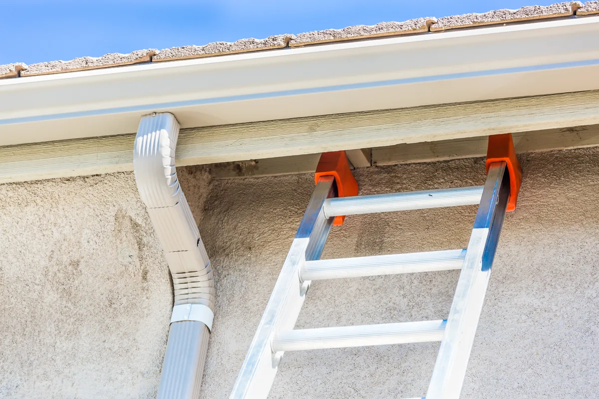 Downspout cleaning in Vancouver, BC — exterior view of a home's downspout and gutter with a ladder in position
